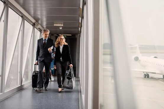 A man and a woman in an airport corridor with carry-on suitcases