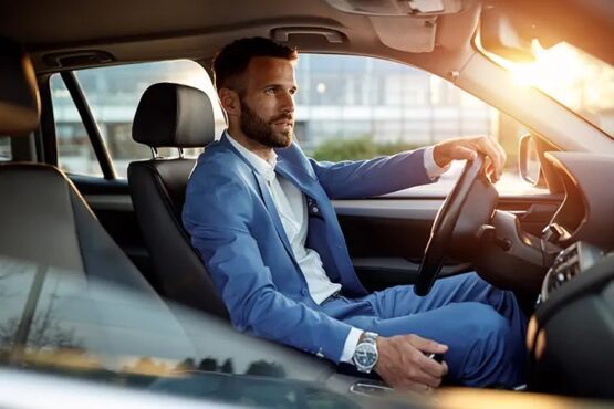 A man in a blue suit sitting behind the wheel of a car